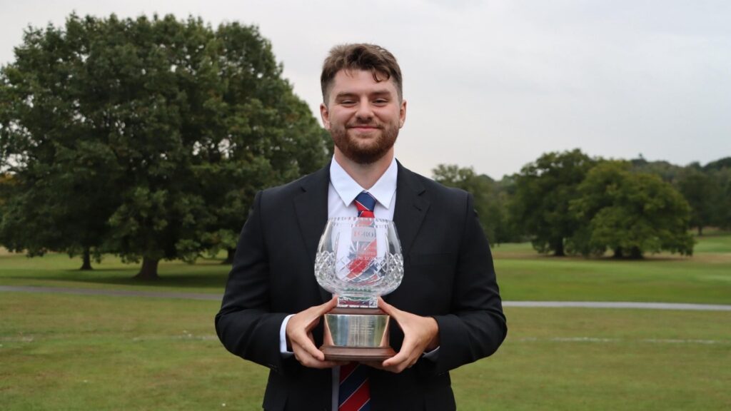 Matt in a suit, smiling to the camera and holding his award