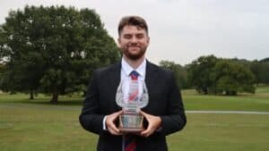 Matt in a suit, smiling to the camera and holding his award