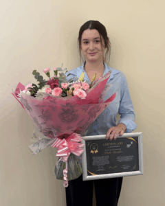 Elodie holding her certificate and some flowers, smiling to the camera